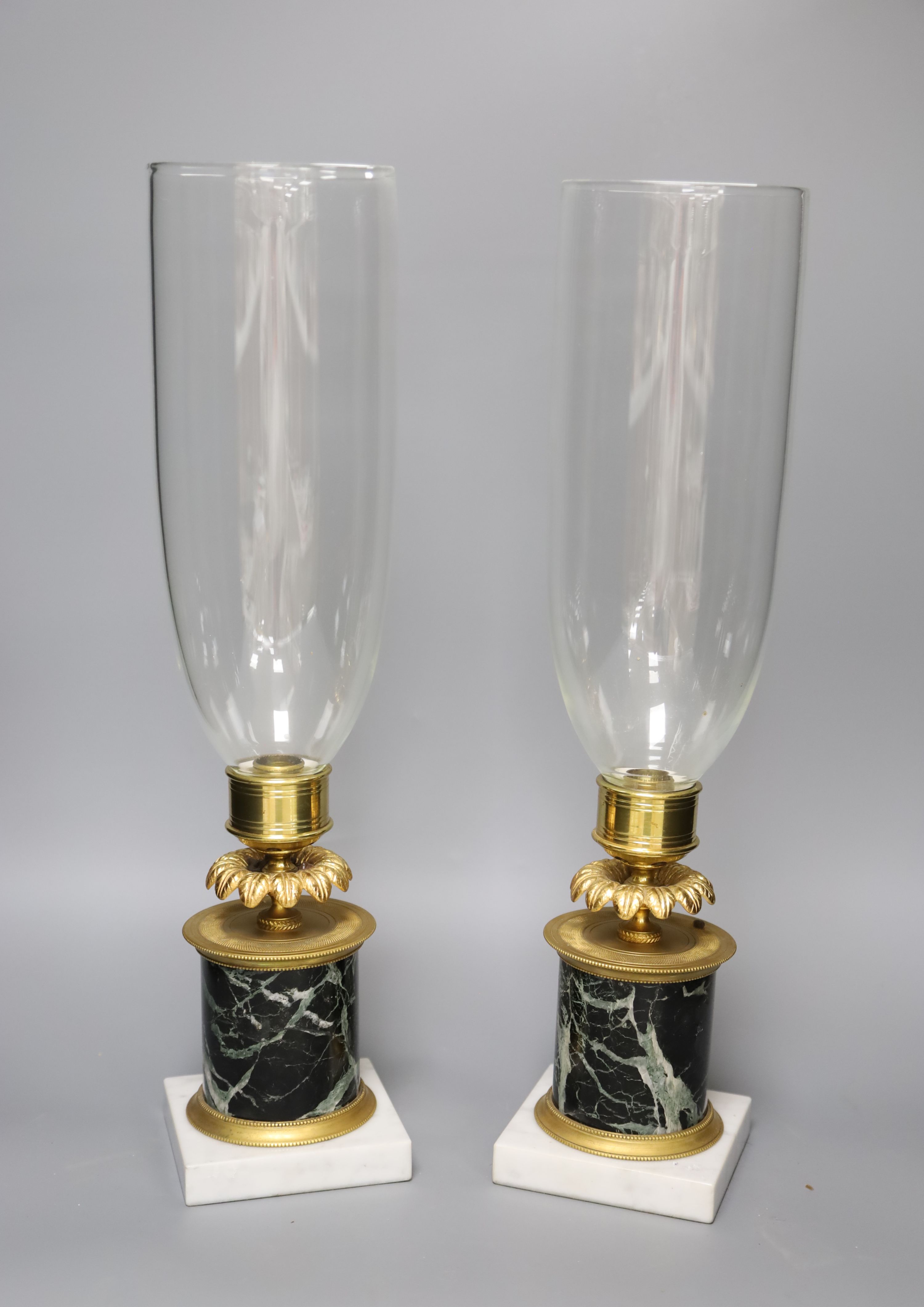 A pair of Regency style ormolu and marble candle lamps, height 48cm to glass storm shades